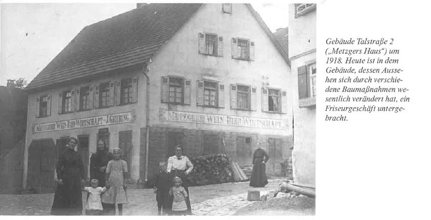 Eine Gruppe von Menschen, darunter Kinder und Erwachsene, steht vor einem alten Gebäude mit der Aufschrift „Metzger's Wein, Bier und Wirtschaft“ in einem historischen Foto um 1918.